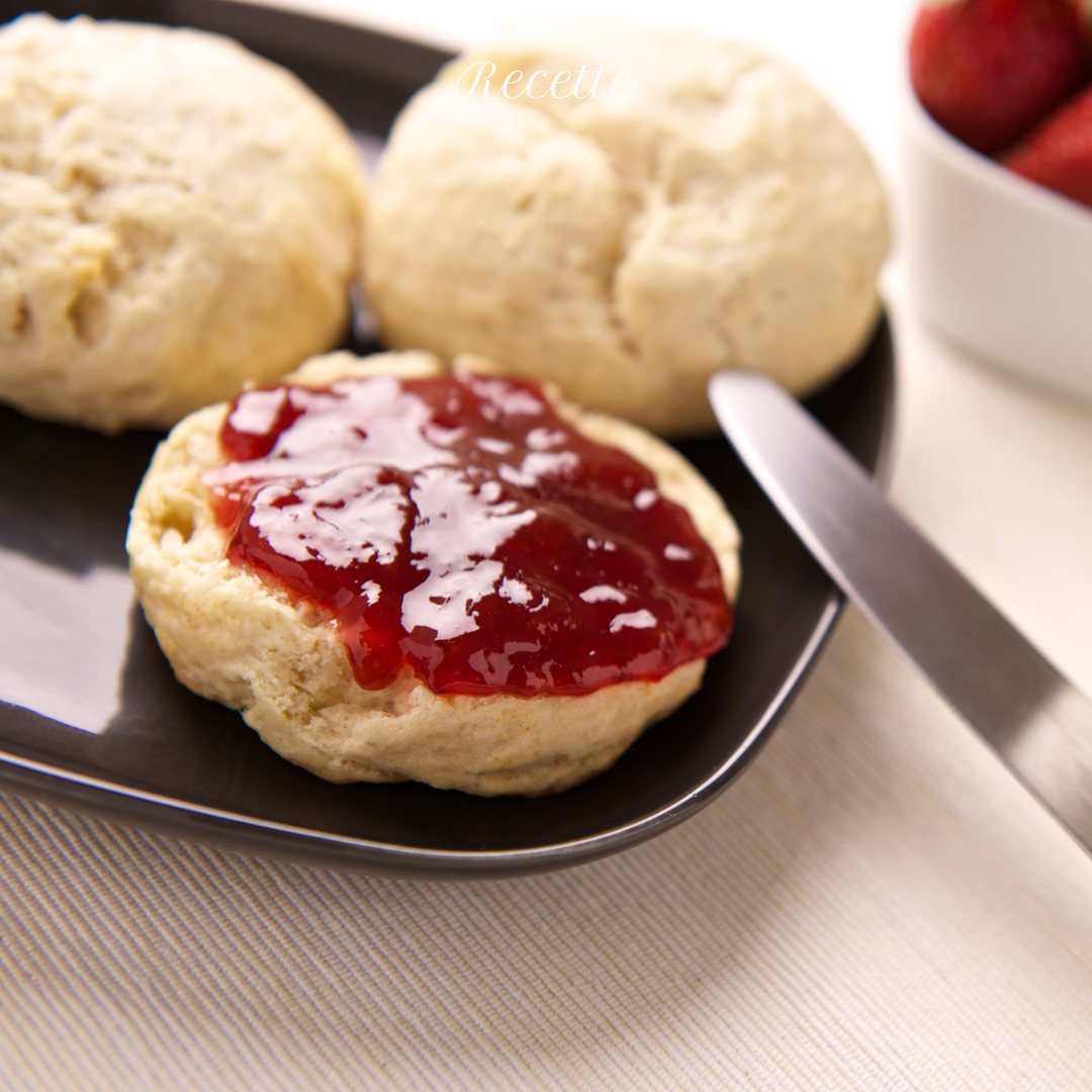 Scones on a plate, with one split and topped with red jam