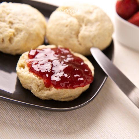 Scones on a plate, with one split and topped with red jam