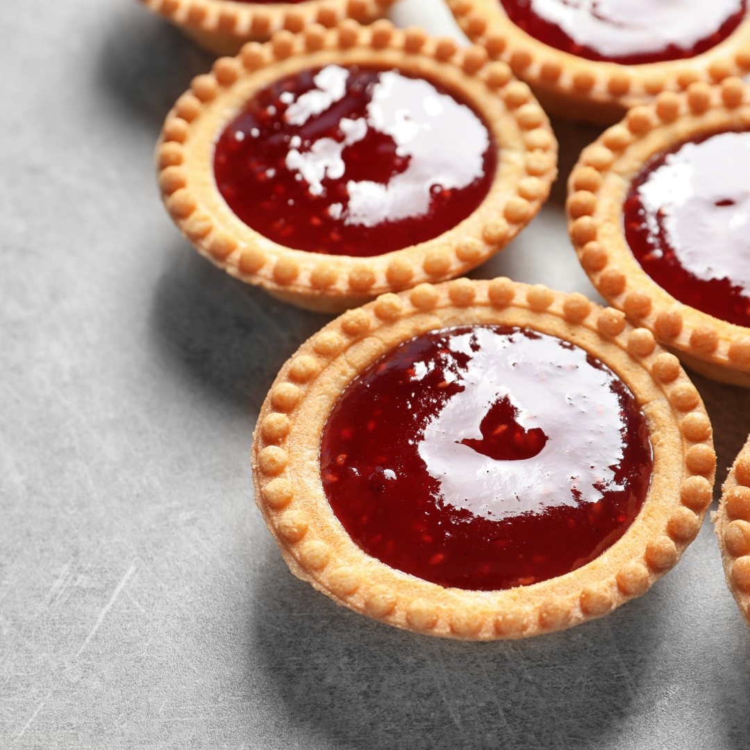 Golden tartlets filled with red jam, arranged on a grey surface